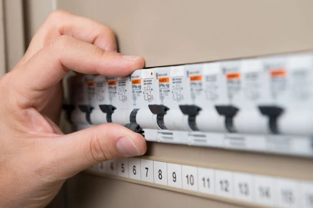 A hand turning on the switchboard button to reset an AC unit