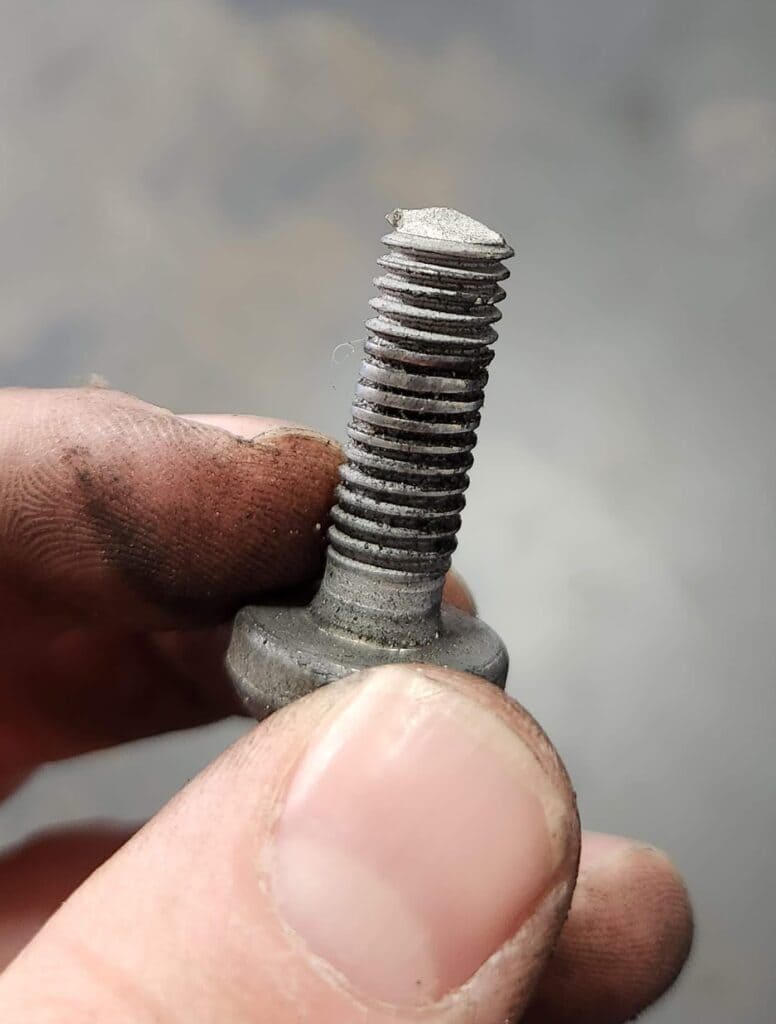 A person holding the mounting bolt of an AC compressor