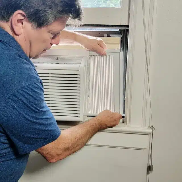 A person seen mounting an ac in a casement window indoors