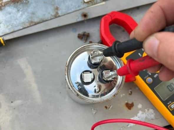 A top view of a person checking the AC capacitor voltage with a multimeter