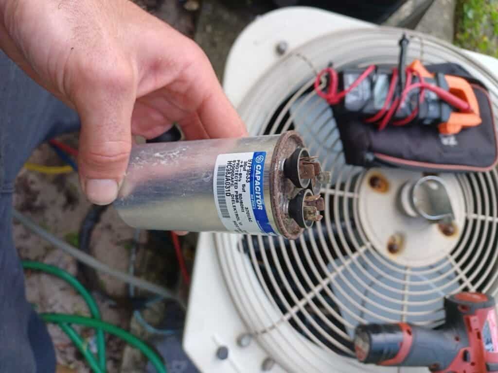 A view of a person holding an AC capacitor out of an air conditioner