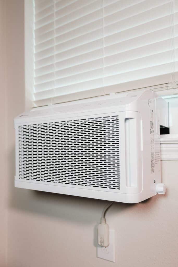 A view of an AC blowing in a window with white blinds