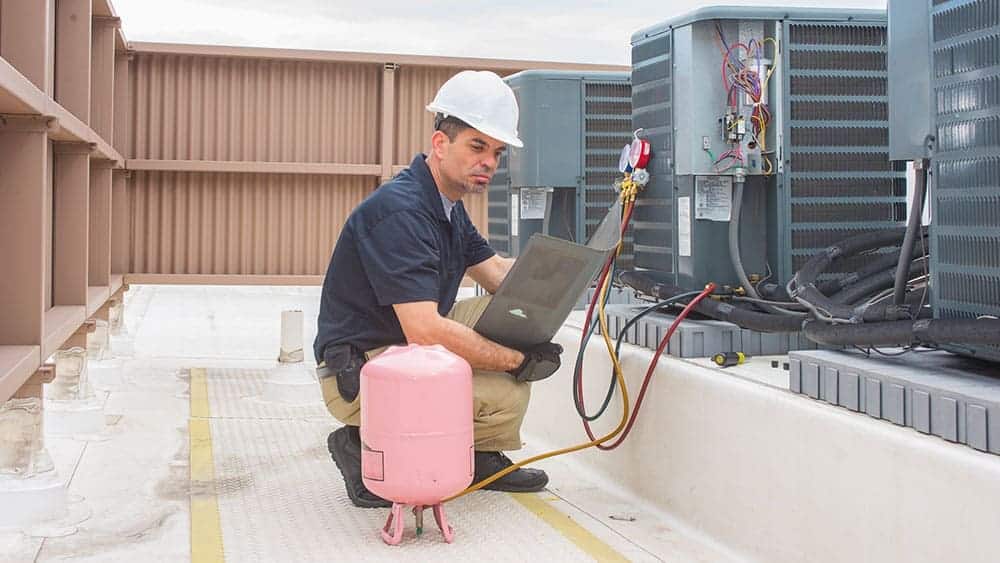 An engineer sitting in front of an AC refrigerant and measuring stats