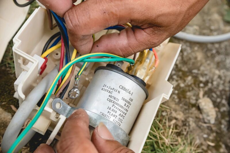 A view of a person dealing with wired to replace a capacitor of an ac