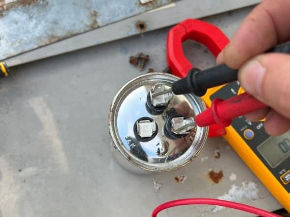 A view of a person testing the ac capacitor with a multimeter