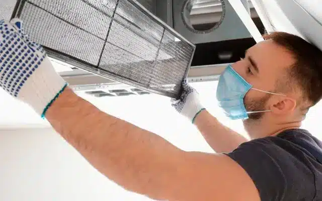 A view of a person with mask on taking out the ac duct to clean