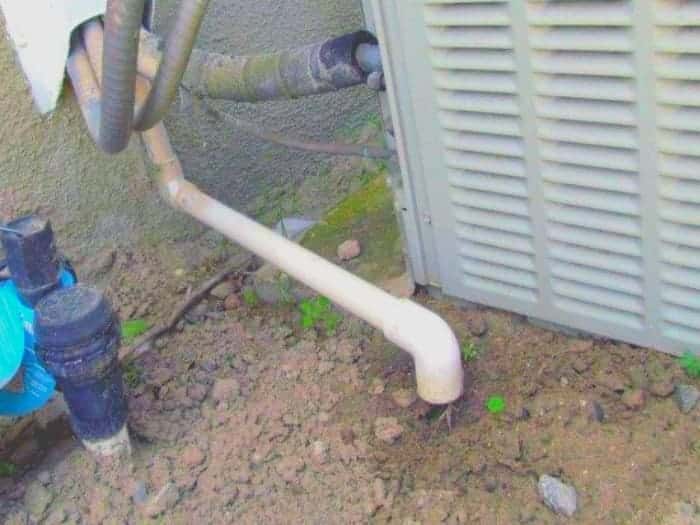 A view of an ac condensate pipe attached in mud outdoors