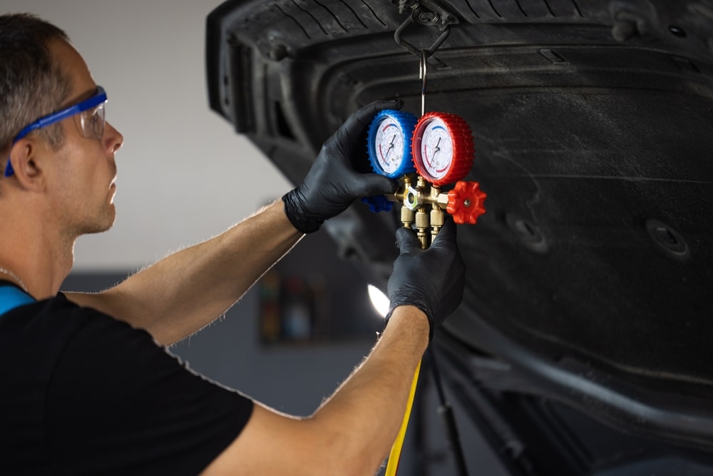 A view of a mechanic holding a manometer to recharge ac