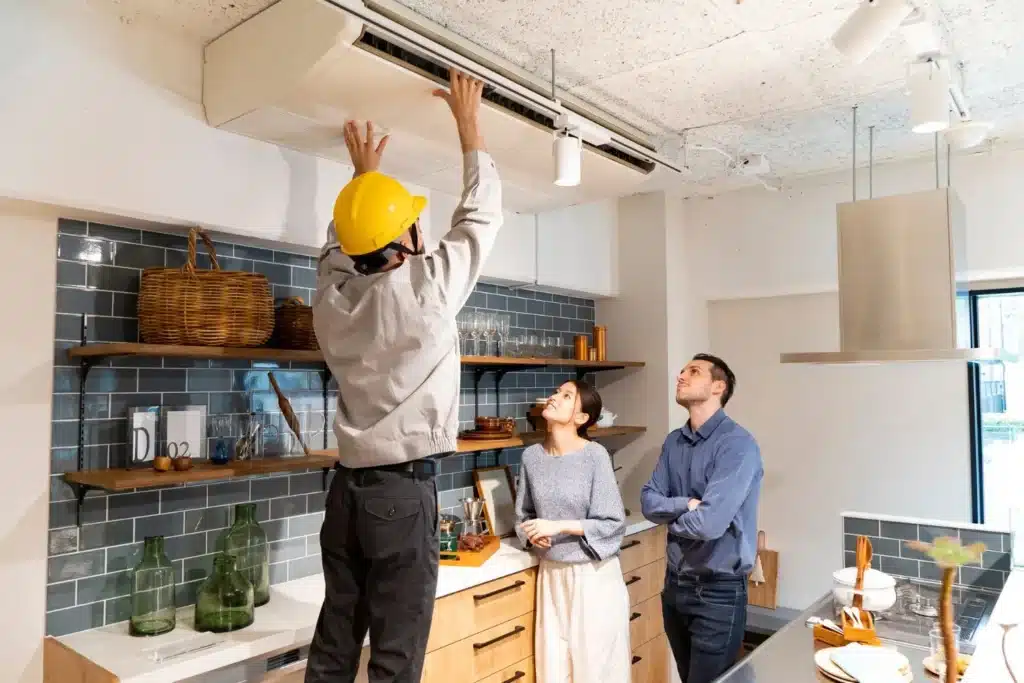 A view of a mechanic recharging an ac with two people standing inside a home