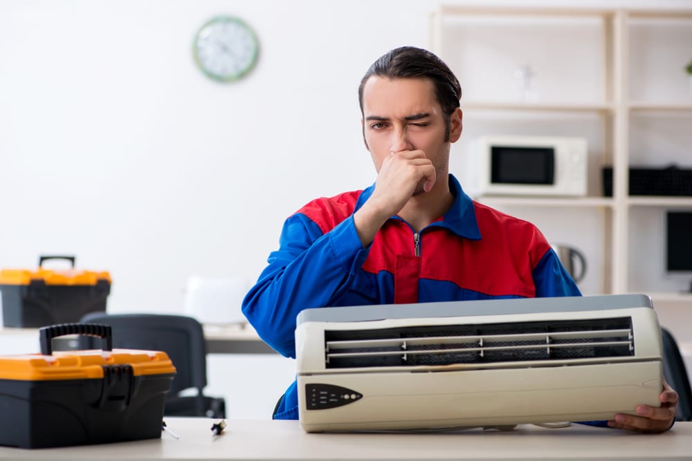 A view of a Hvac technician fixing an ac with hands on his nose