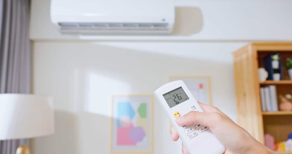 A view of an aircon inside a room with a person holding an ac remote